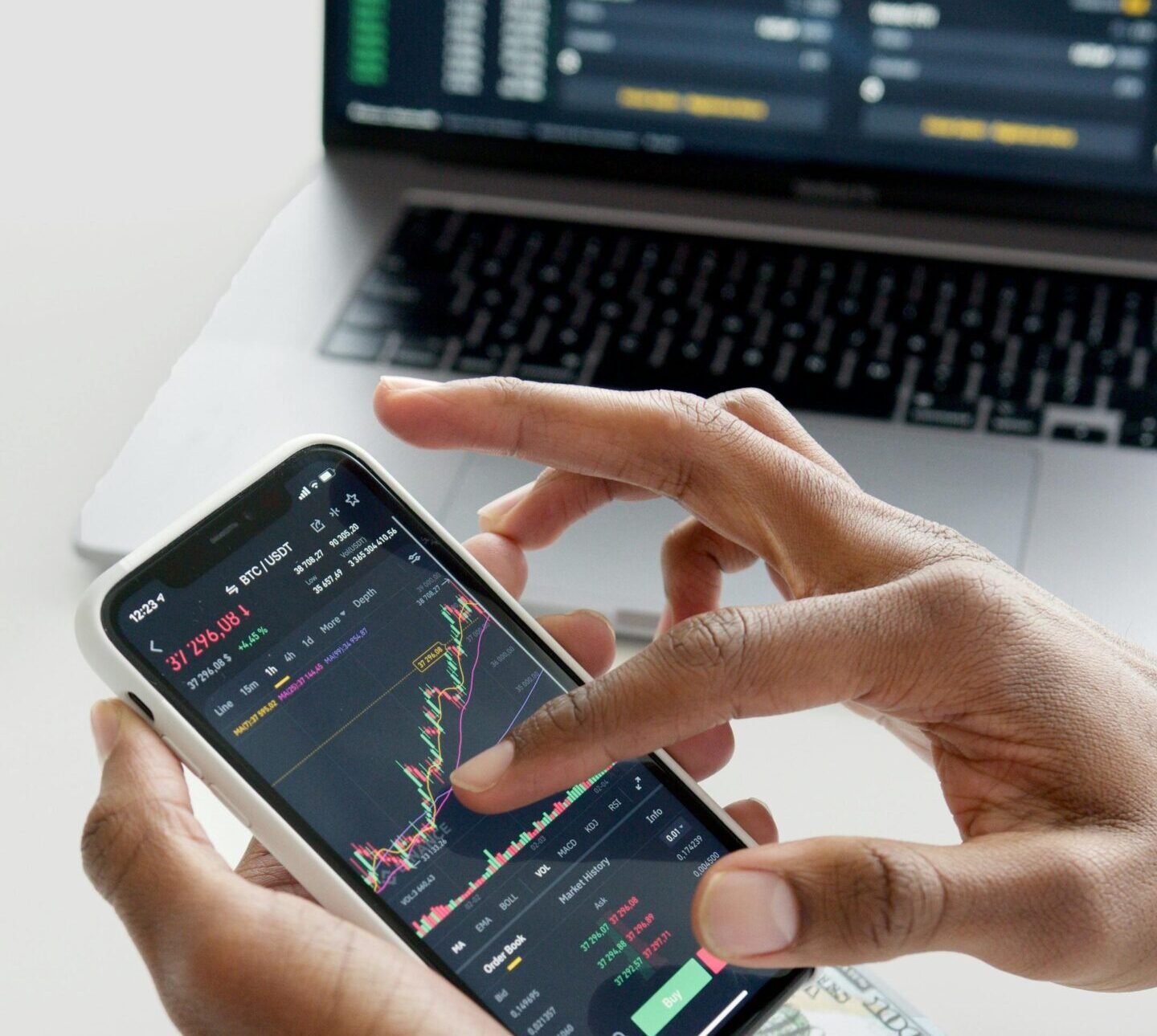 Hands using smartphone trading app with charts, dollar bills in background.