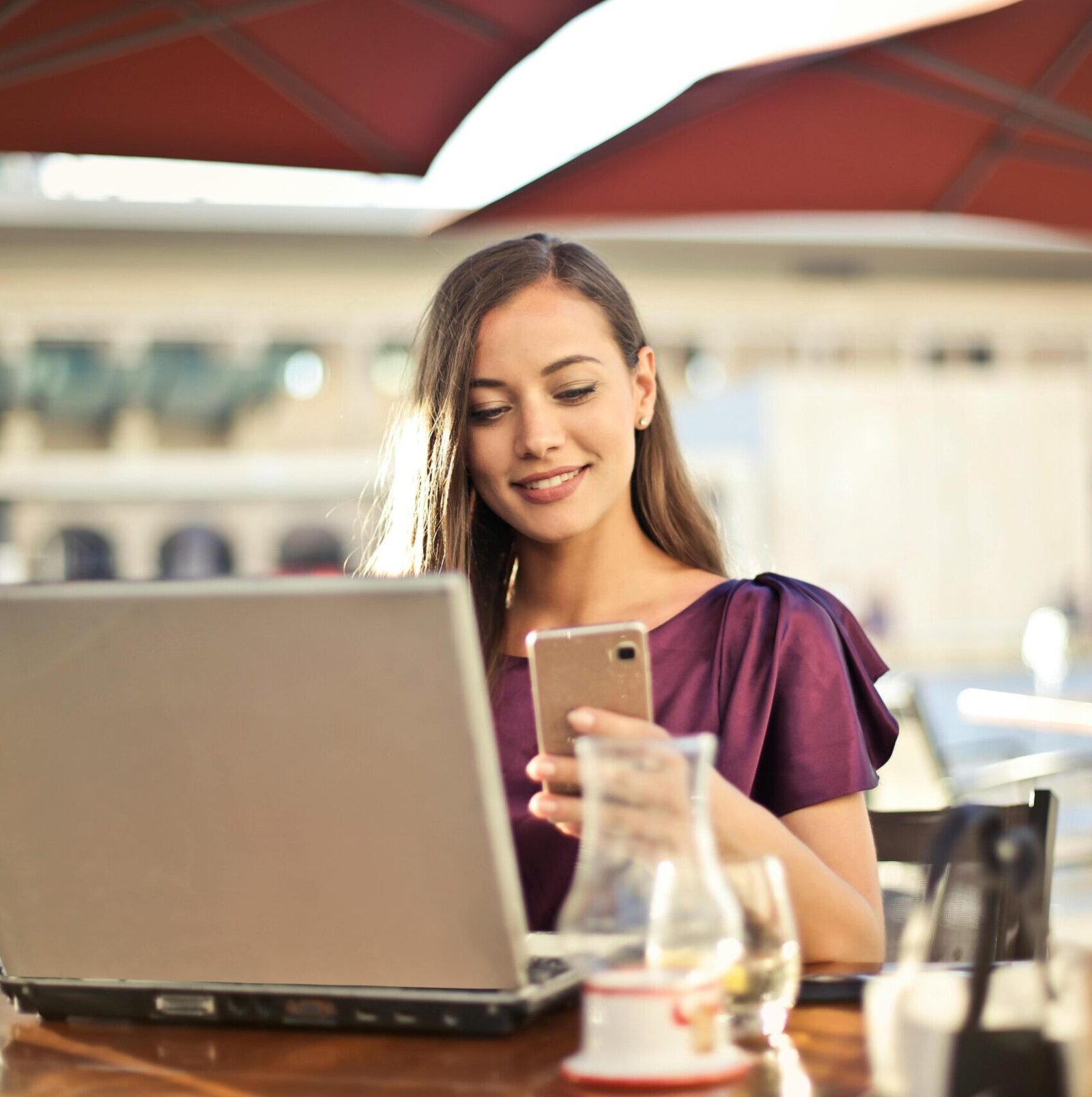 Woman enjoying remote work at a café, using a laptop and smartphone.